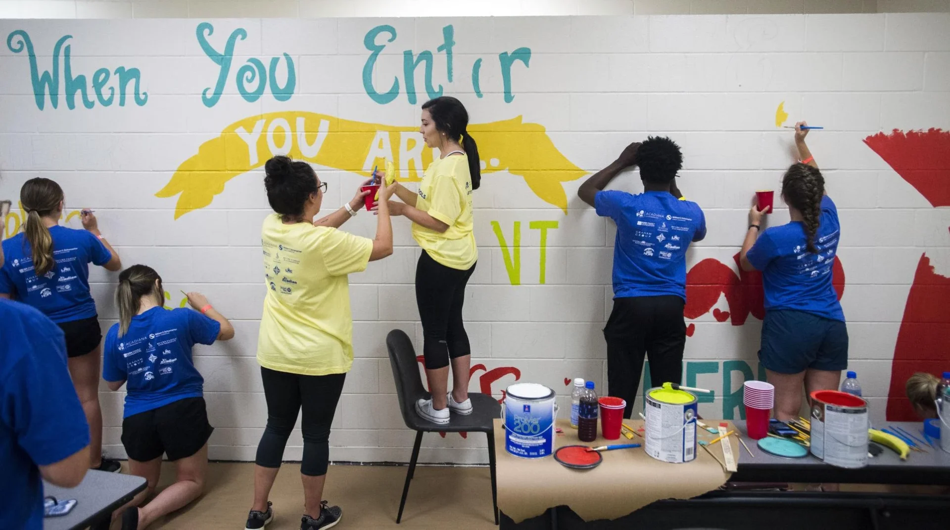 Group of people painting at the wall.